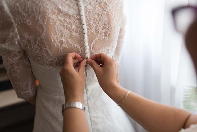 someone helping a bride zip up a lace wedding gown