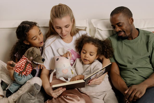 Family of four lying in bed and reading a book together