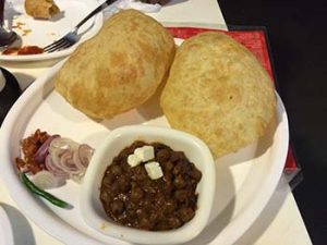 A plate of Chhole Bhature with a side of pickles, onions and green chili 