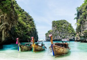 A beach with large rocks in the ocean and three boats