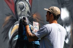 Artist in a cap spray-painting a detailed animal mural on an urban wall.