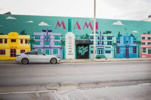 Colorful mural depicting the Miami skyline on a building's wall, with a car parked in front.