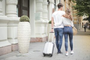 A couple carrying their suitcases down the street.