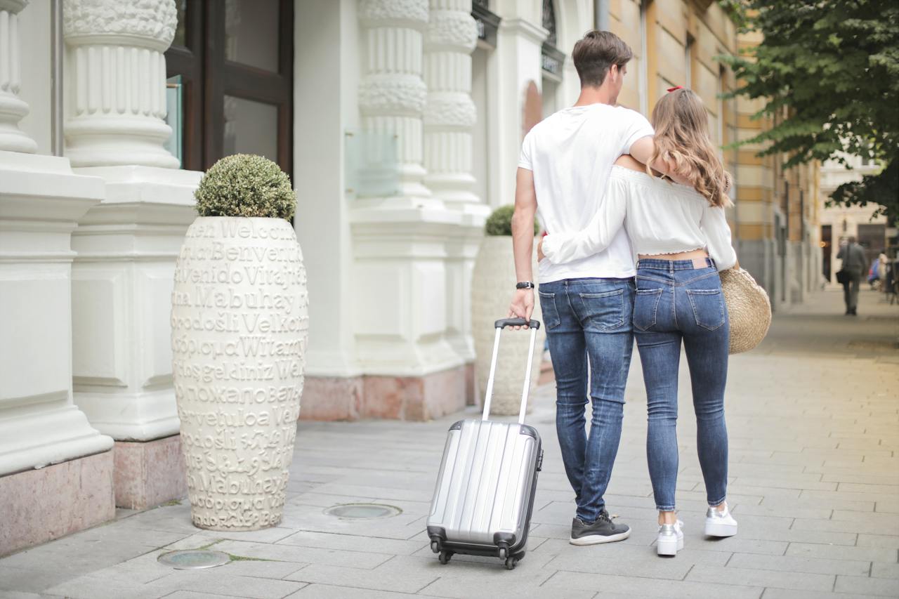 A couple carrying their suitcases down the street. 