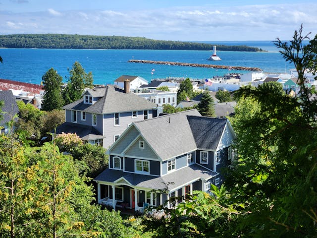 View of a scenic waterfront with houses nestled among trees, showcasing the natural beauty of Mackinac Island and the surrounding coastline