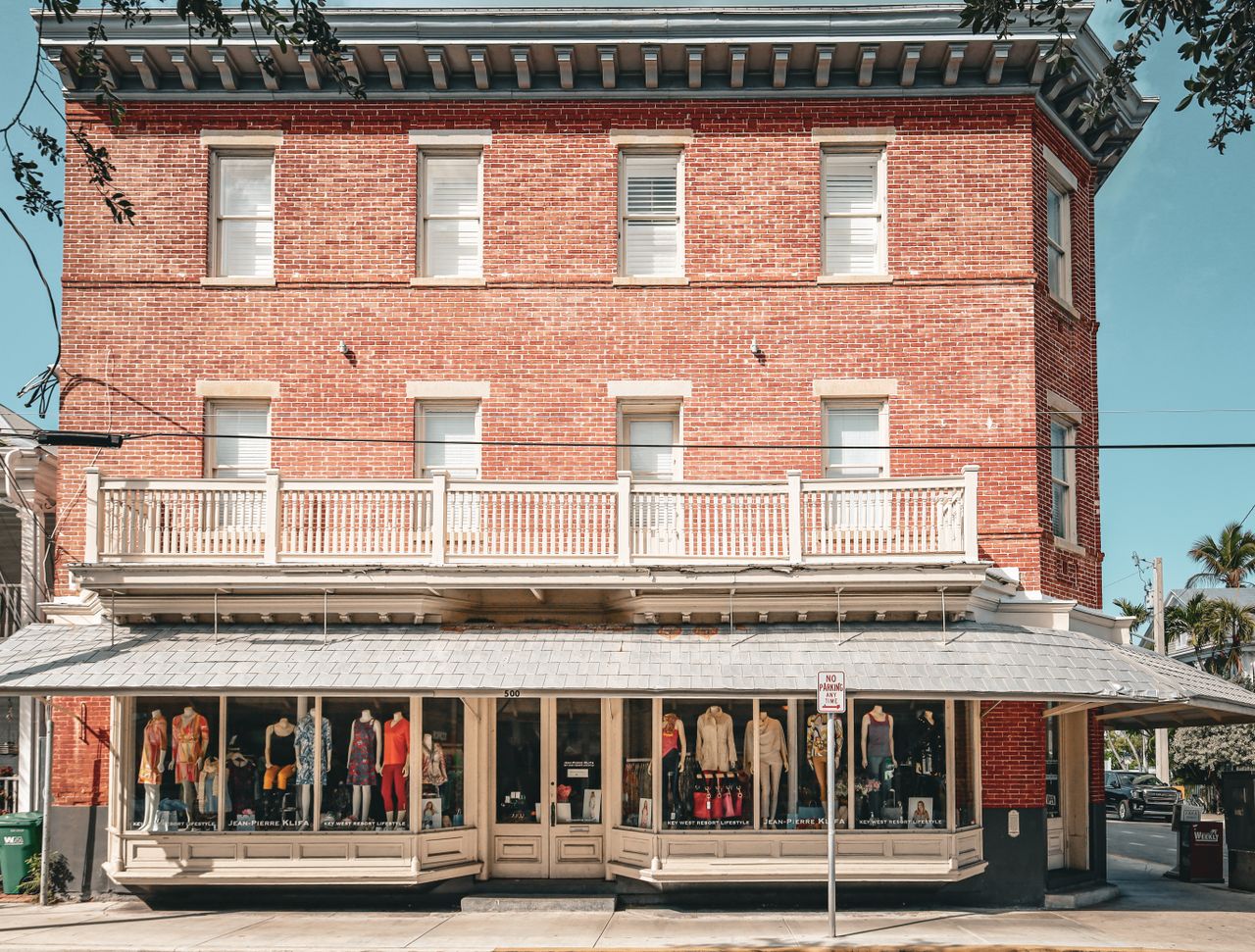 Historic three-story red brick storefront building with a wraparound white balcony and ground-floor boutique awning on a small-town Main Street.
